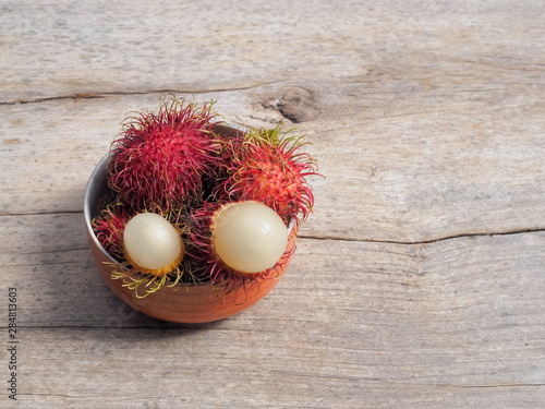 Top view of fresh Rambutan fruit (Nephelium lappaceum) in a bowl on wood texture background.