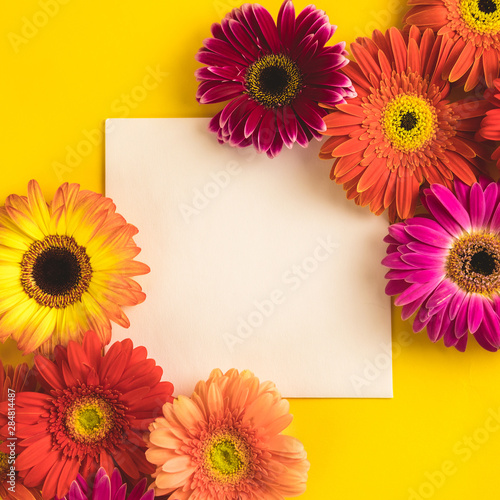 Bright beautiful gerbera flowers and paper card on a sunny yellow background. Mother's Day, Valentine holiday. Place for text, lettering or product. View from above, Copy space. Flatlay.