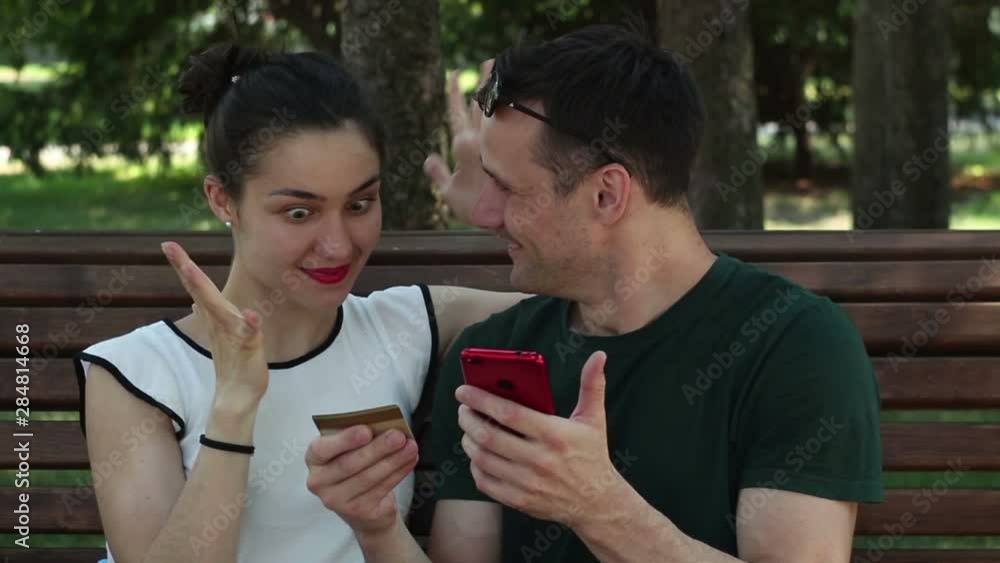 Young couple in love make purchases on the Internet with the help of a smartphone and a credit card. A young couple in love enter credit card details into a smartphone to pay for purchases on the Young couple in love make purchases on the Internet with the help of a smartphone and a credit card. A young couple in love enter credit card details into a smartphone to pay for purchases on the