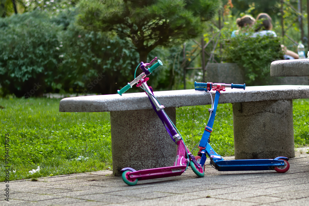 Two non-electric children's scooters parked on a concrete bench in the park. Two non-electric children's scooters parked on a concrete bench in the park.