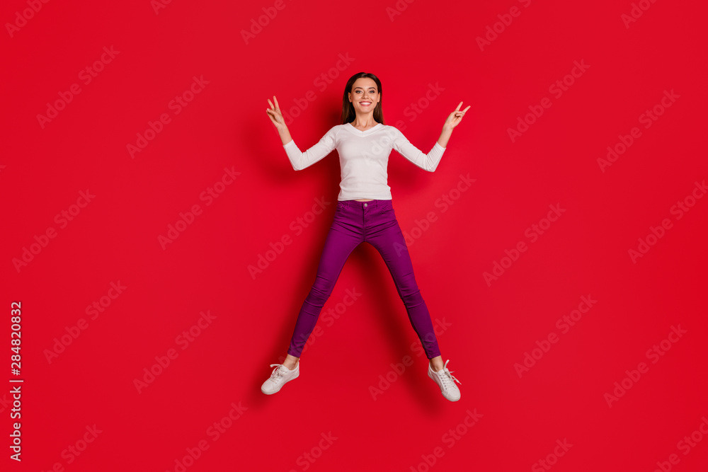 Full length body size photo of jumping nicely looking childish girl giving everyone of you v-sign while isolated with red background