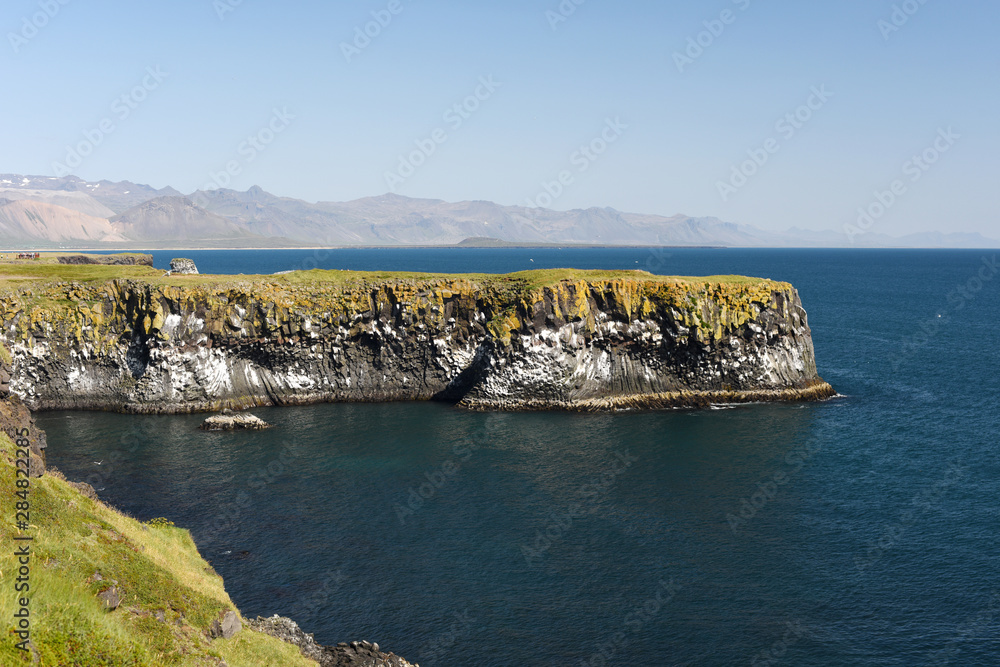 West coast sea cliffs of Snaefellsnes Peninsula on Iceland.Pure blue water with high cliffs above sea. Beautiful colourful scenic view of basalt rock reef.