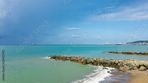 Sea shore with stone breakwaters on a sunny summer day with ships on the horizon and cloudy sky. © Vit-Vit