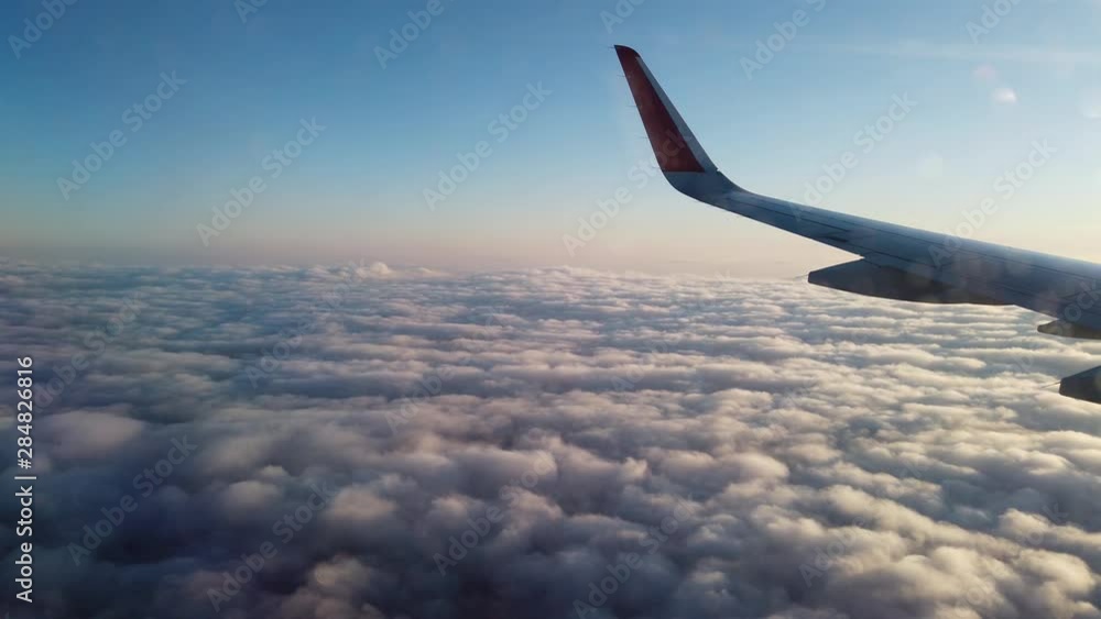 View from the porthole of an airplane. Flying at high altitude over an even layer of clouds. Early morning.