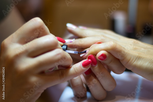 Female nail painting. Manicurist applying transparent varnish on little finger nail during final step of her work.