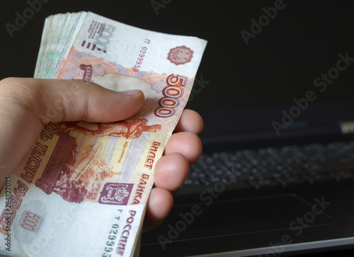 Online loans. Man hand holding a bundle of Russian money. Laptop in the background.