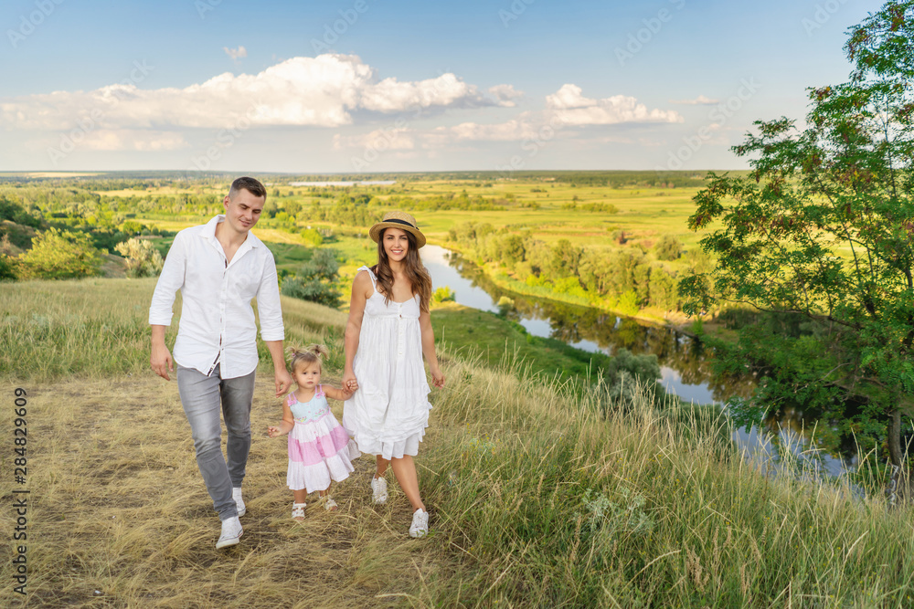young mom and dad lead their daughter by the hand while walking in nature