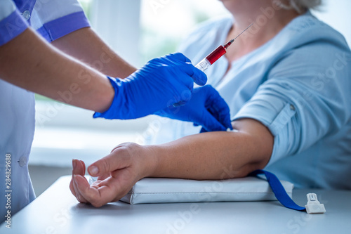 Nurse in rubber blue medical gloves takes blood from a vein for laboratory test.