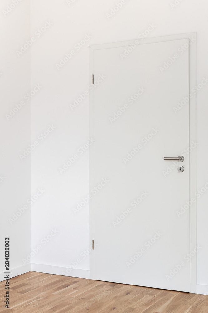 Closed white door with a gray chrome handle and keyhole with key against a white wall in the room - obrazy, fototapety, plakaty 