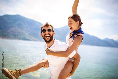 Handsome young man giving piggyback ride to girlfriend on beach. Romantic young couple enjoying summer holidays.
