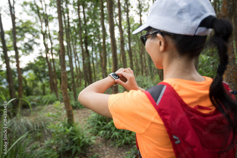 Asian woman ultramarathon runner set the sports watch before running at tropical rainforest trail