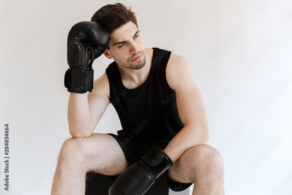 Strong young sports man boxer in gloves sitting and have a rest isolated over white background.