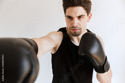 Strong serious young sports man boxer in gloves make exercises isolated over white background. © Drobot Dean