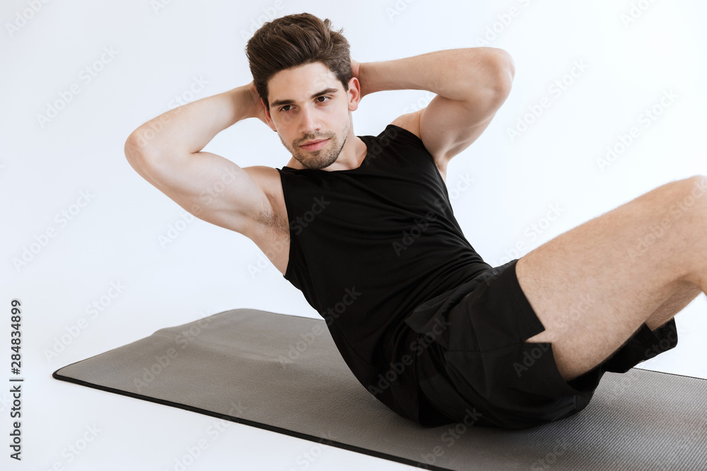 Fototapeta premium Concentrated strong young sports man make abs exercise isolated over white background.