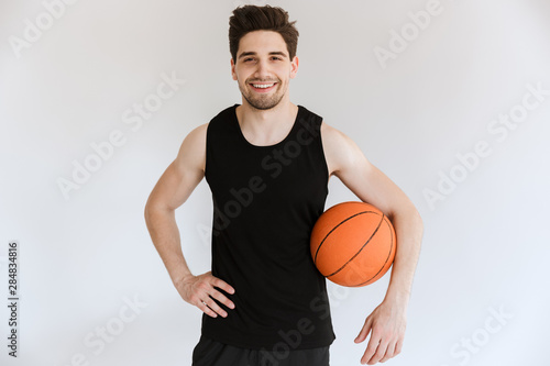 Smiling strong young sports man basketball player holding ball isolated over white background. © Drobot Dean