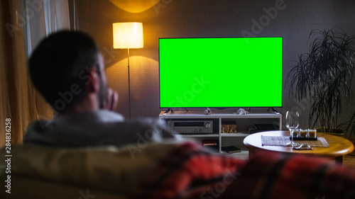 Bilde på lerret In the Evening Back View of a Middle Aged Man Sitting on a Couch Watching Big Flat Screen TV