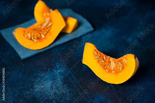 Pieces of raw sliced pumpkin lie on a concrete table
