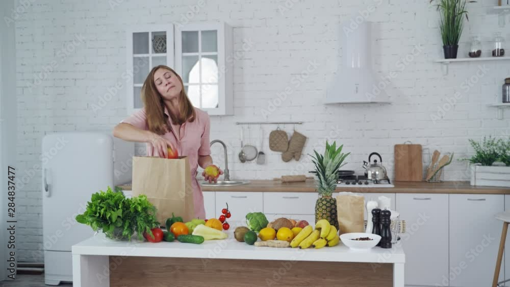 Healthy food on a kitchen table. Beautiful woman taking out fresh apples from shopping bag. Loving mom cares about nutrition. Healthy food on a kitchen table. Beautiful woman taking out fresh apples from shopping bag. Loving mom cares about nutrition.