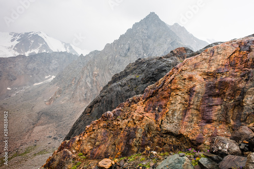 Bright large red stone with purple streaks. A pyramid-shaped mountain and a mountain peak in snow and a glacier. Gigantic sticking out stone. Mountain valley of Altai nature. An admixture of iron ore 