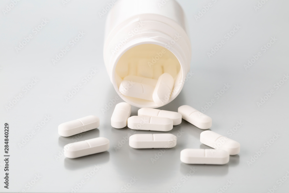 Scattered tablets made of white plastic bottles on a light grey background Scattered tablets made of white plastic bottles on a light grey background