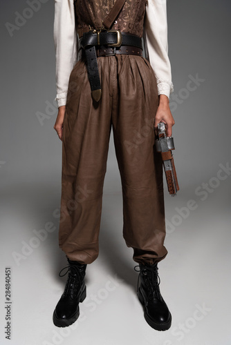cropped view of steampunk woman holding vintage pistol on grey