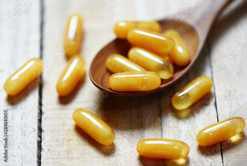 Photography Royal jelly capsules in wooden spoon and wood table background - Yellow capsule