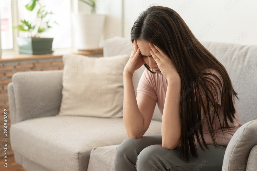 Asian woman are holding their hands to the head in pain on the sofa at home, Young women have severe headaches from migraines, Health and illness concept Asian woman are holding their hands to the head in pain on the sofa at home, Young women have severe headaches from migraines, Health and illness concept