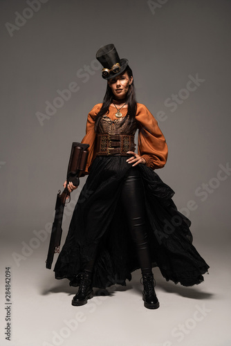 full length view of attractive steampunk woman holding guy on grey