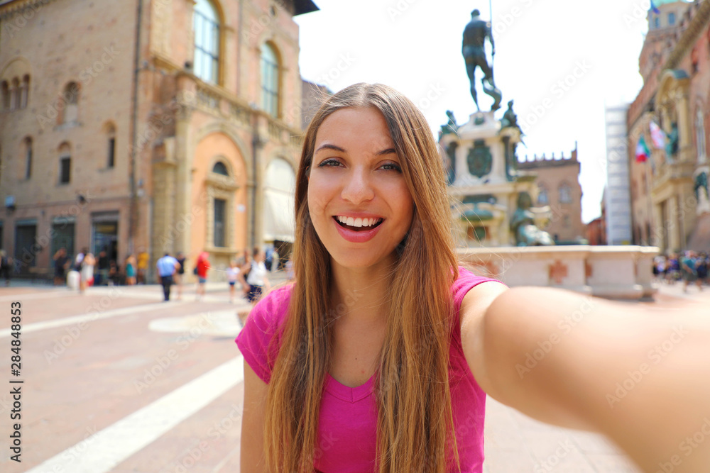 Beautiful Italy. Attractive smiling young woman take self portrait in Piazza del Nettuno square Bologna city, Italy.