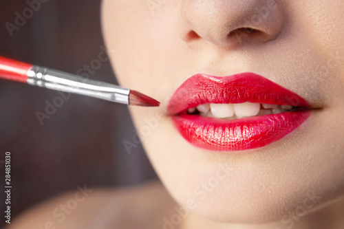 Female lips with red lipstick close-up. Makeup artist applying lipstick with a brush