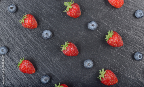 Flat lay view at ripe bilberry and strawberries on slate stone tray closeup