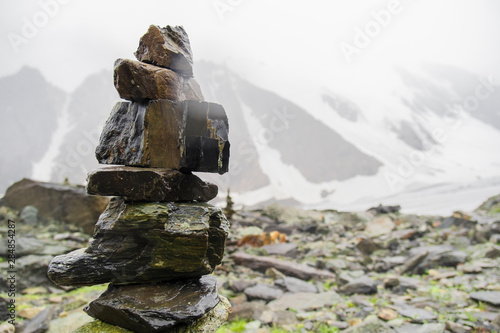 Mountain Altai. Cairn on top of a large mountain. Mountain peaks in the misty clouds. Beautiful views of high snow-capped mountains and a glacier on a tourist trip through the nature of Altai land. © Sanklinarika