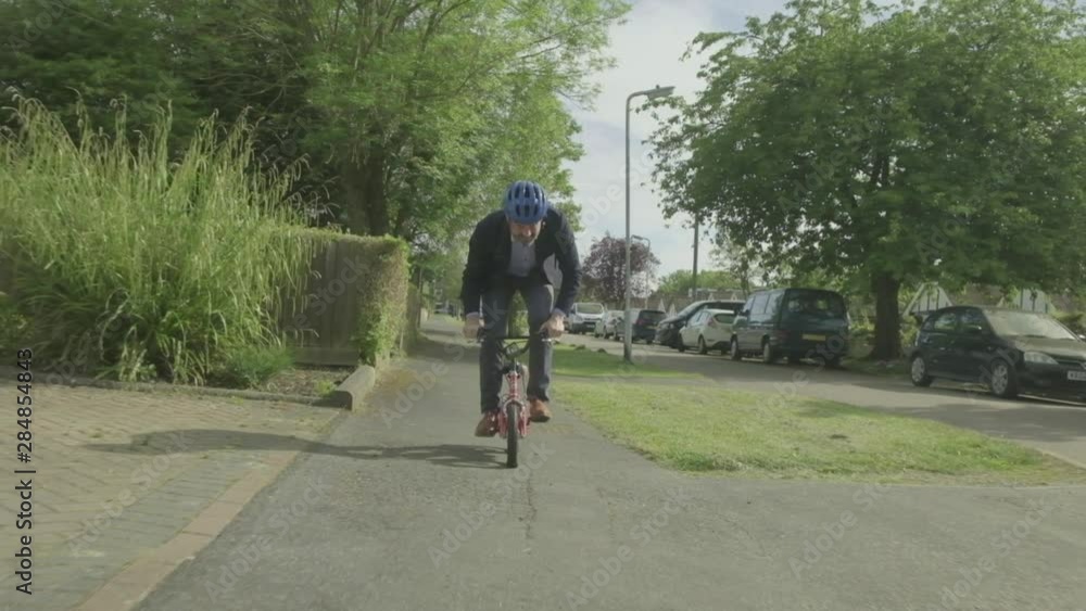 Steady cam view of a caucasian businessman cycling on a child's bike themes of contrasts carefree humour young at heart Steady cam view of a caucasian businessman cycling on a child's bike themes of contrasts carefree humour young at heart