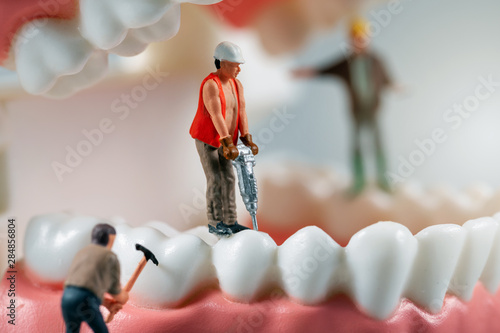 dental treatment concept - miniature figurines of construction workers on teeth model