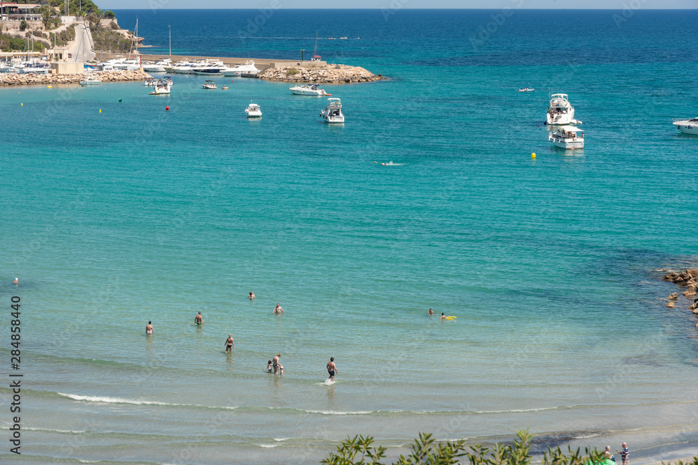 Orihuela Costa, Spain - June 16, 2018: People sunbathing and swiming at the Cala Capitan beach in the Cabo Roig, popular place for holidaymakers. Province of Alicante. Costa Blanca. Spain Orihuela Costa, Spain - June 16, 2018: People sunbathing and swiming at the Cala Capitan beach in the Cabo Roig, popular place for holidaymakers. Province of Alicante. Costa Blanca. Spain