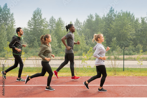 Side view of four young sportsmen and sportswomen running down racetracks