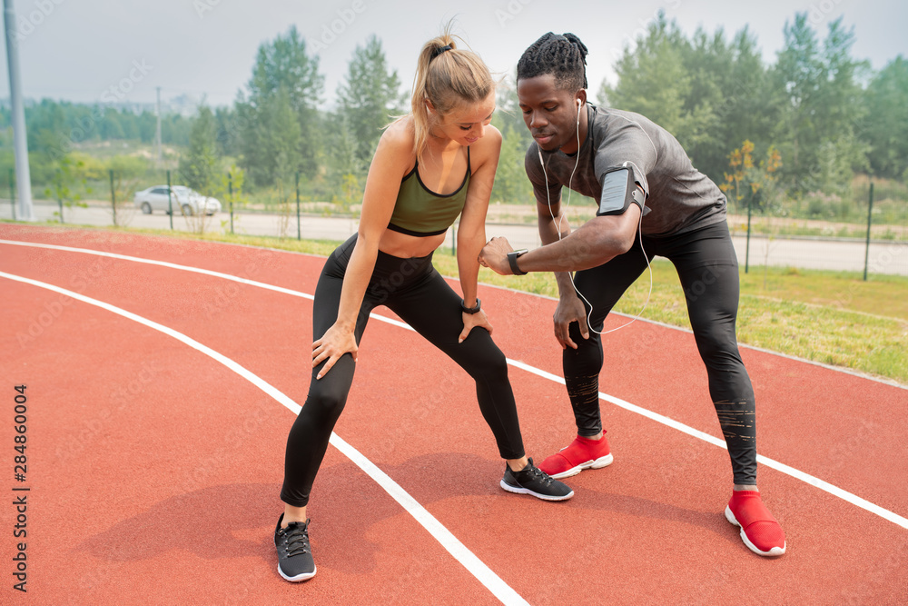 Young athlete showing time to active girl while both standing on start line Young athlete showing time to active girl while both standing on start line