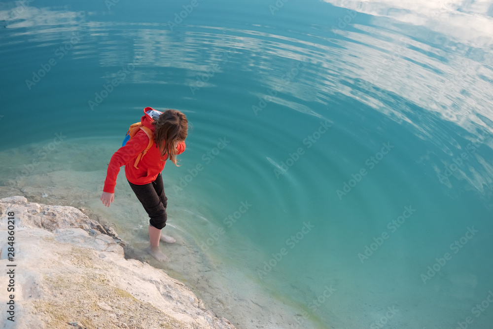 Fototapeta premium Barefoot caucasian kid weared in red hoodie plays in blue sea water