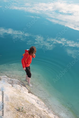 Barefoot caucasian kid weared in red hoodie walks in blue sea water © Kiryl Lis