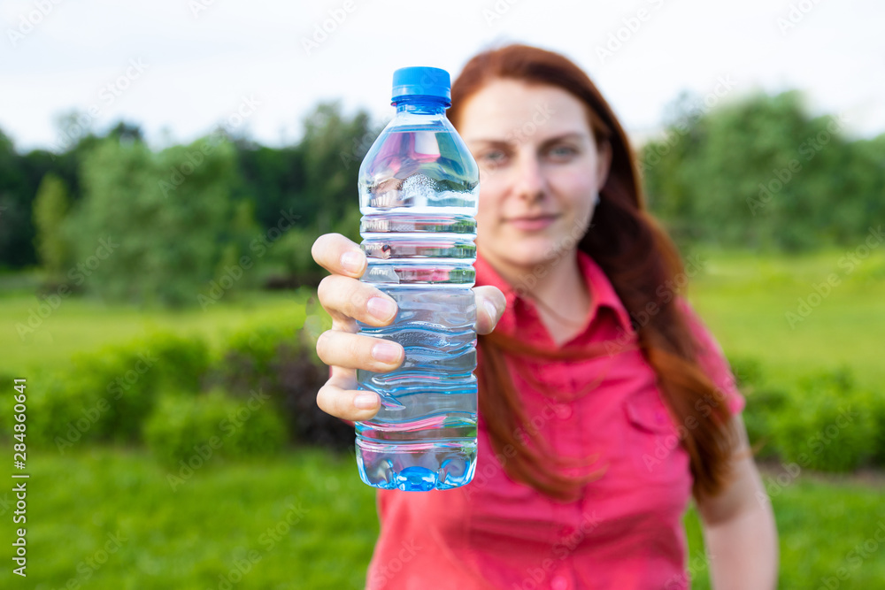 Young girl in bright summer clothes holds a plastic bottle of water on the background of the park Young girl in bright summer clothes holds a plastic bottle of water on the background of the park