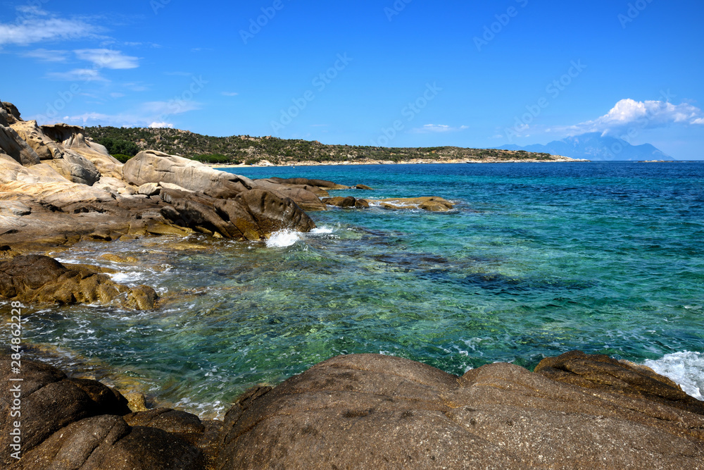 Beautiful seascape with stones and translucent water and the clouds in the blue sky