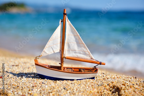Photography Miniature toy sailboat on the beach against the background of the sea and waves