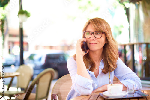 Smiling confident woman talking with somebody on her mobile phone while sitting in cafe on the street