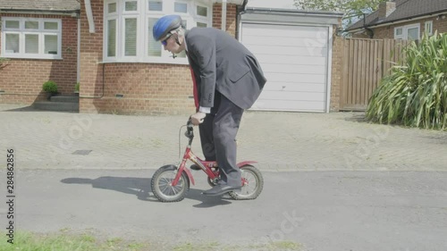 Steady cam view of a caucasian businessman cycling on a child's bike themes of contrasts carefree humour young at heart photo