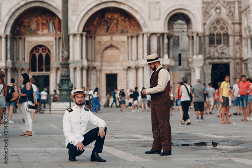 Two young men in vintage suits stand on Piazza San Marco square in Venice, Italy