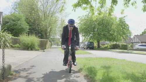 Steady cam view of a caucasian businessman cycling on a child's bike themes of contrasts carefree humour young at heart