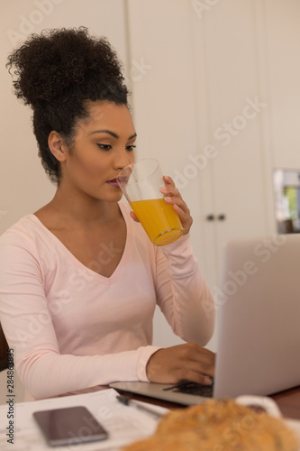 Woman having orange juice while using laptop at home