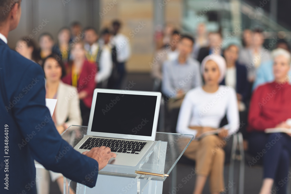 Businessman using laptop while speaking at a business seminar Businessman using laptop while speaking at a business seminar