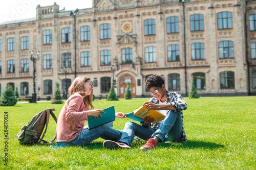 Valokuva Smiling African American student with glasses and with books and girl have fun chatting near college