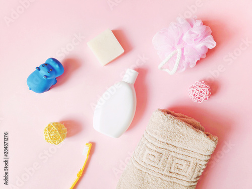 Flat lay photo baby care products on a pink background. Shampoo, soap, toothbrush, beige towel and rubber toy hippo